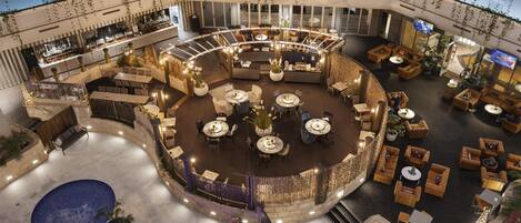 A spacious indoor atrium with multiple seating areas, a central bar, and a pool.