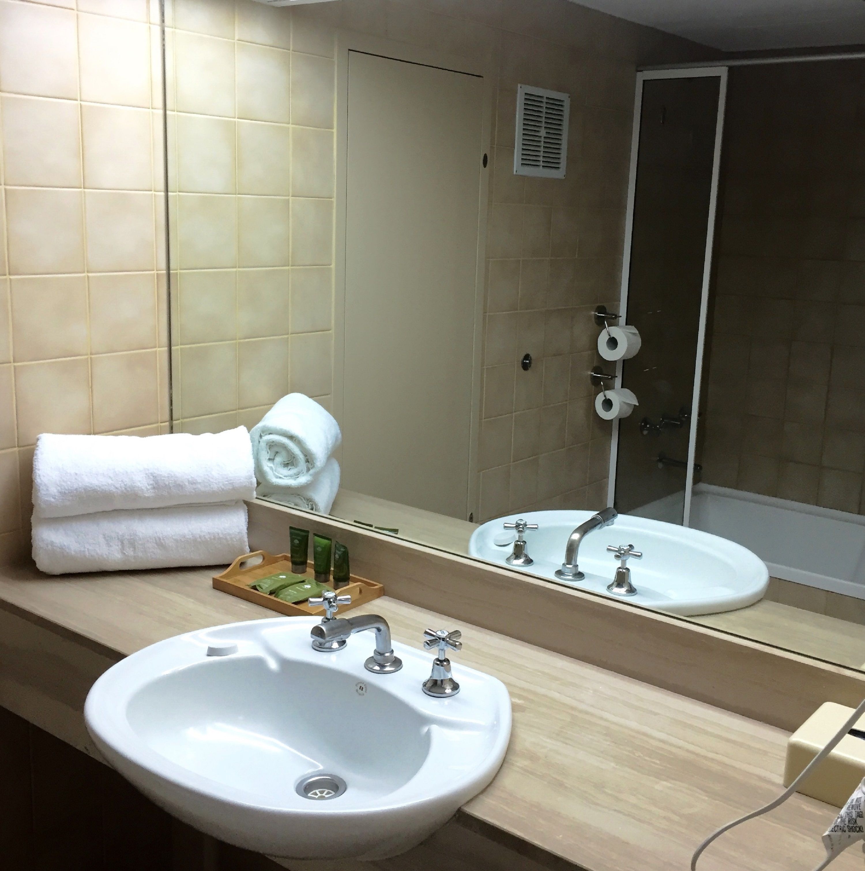 A bathroom with a sink, mirror, towels, and toiletries.