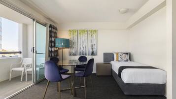 Een hotelkamer met een bed, twee stoelen, een klein tafeltje, een lamp en een schilderij aan de muur.