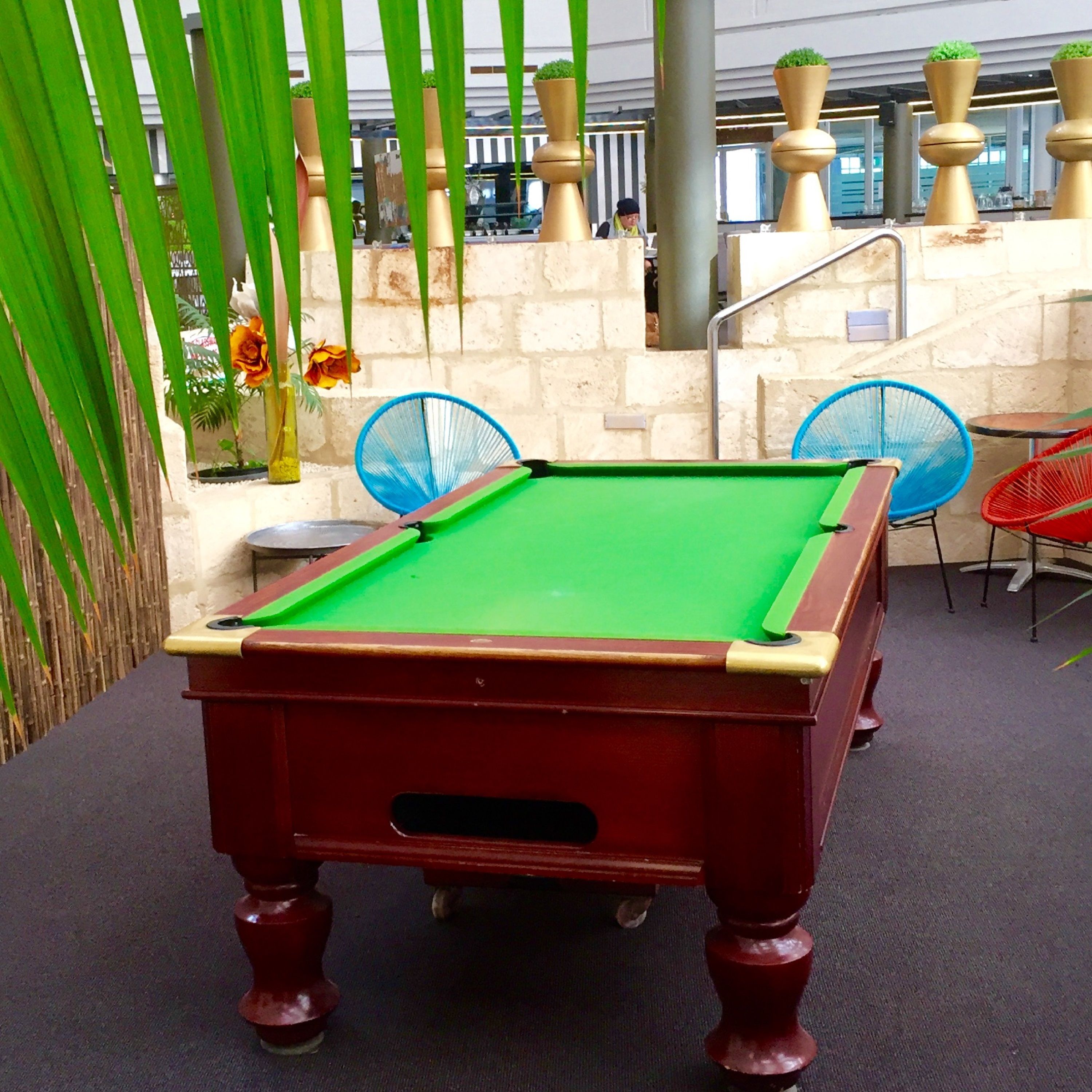 A pool table in an indoor setting with a stone wall and potted plants in the background.