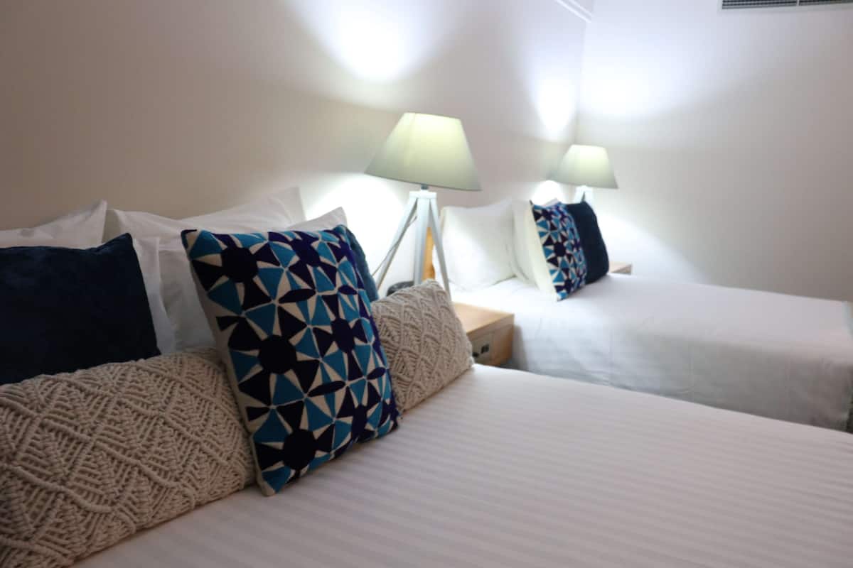 A hotel room with two beds, each with a white bedspread and patterned pillows. There are two bedside lamps on wooden nightstands.
