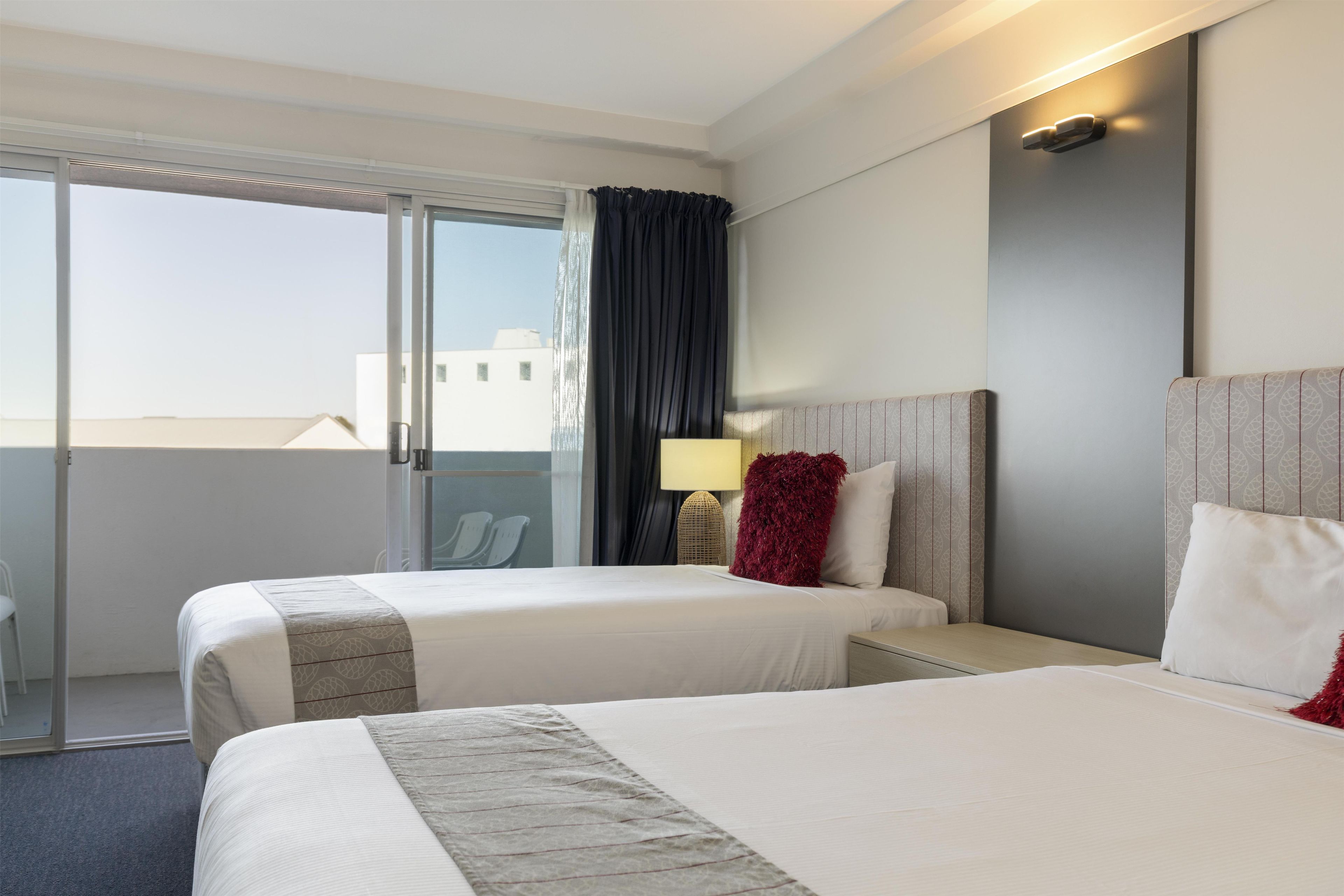 A hotel room with two beds, a large window, and a view of buildings outside.