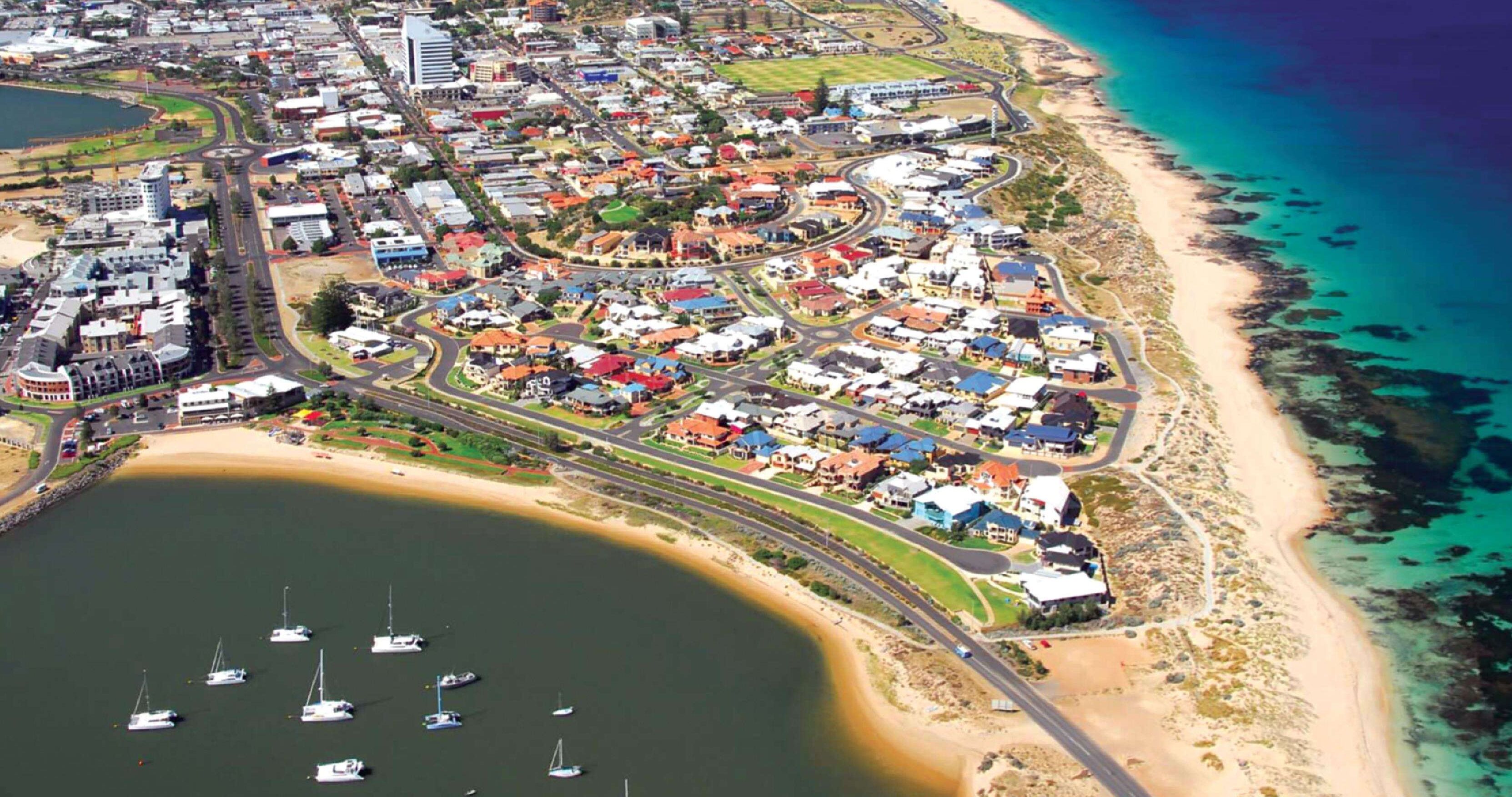 An aerial view of a coastal town with residential areas, a beach, and boats in the water.