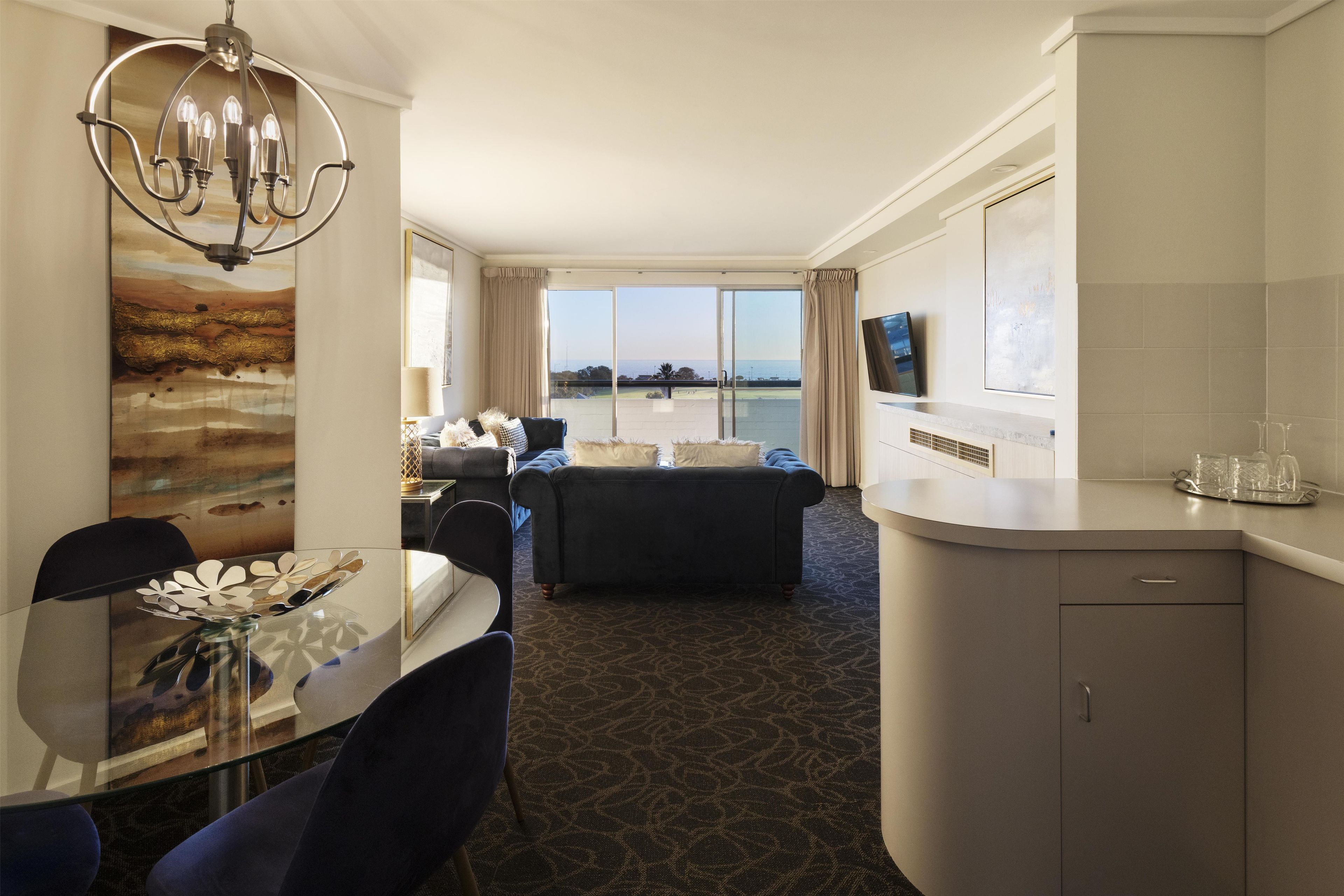 A hotel room with a dining area, a sofa, a TV, and a view of the sea.