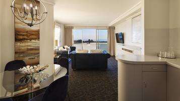 A hotel room with a dining area, a sofa, a TV, and a view of the sea.