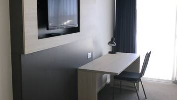 A modern hotel room with a built-in TV, a desk, a chair, and a lamp.