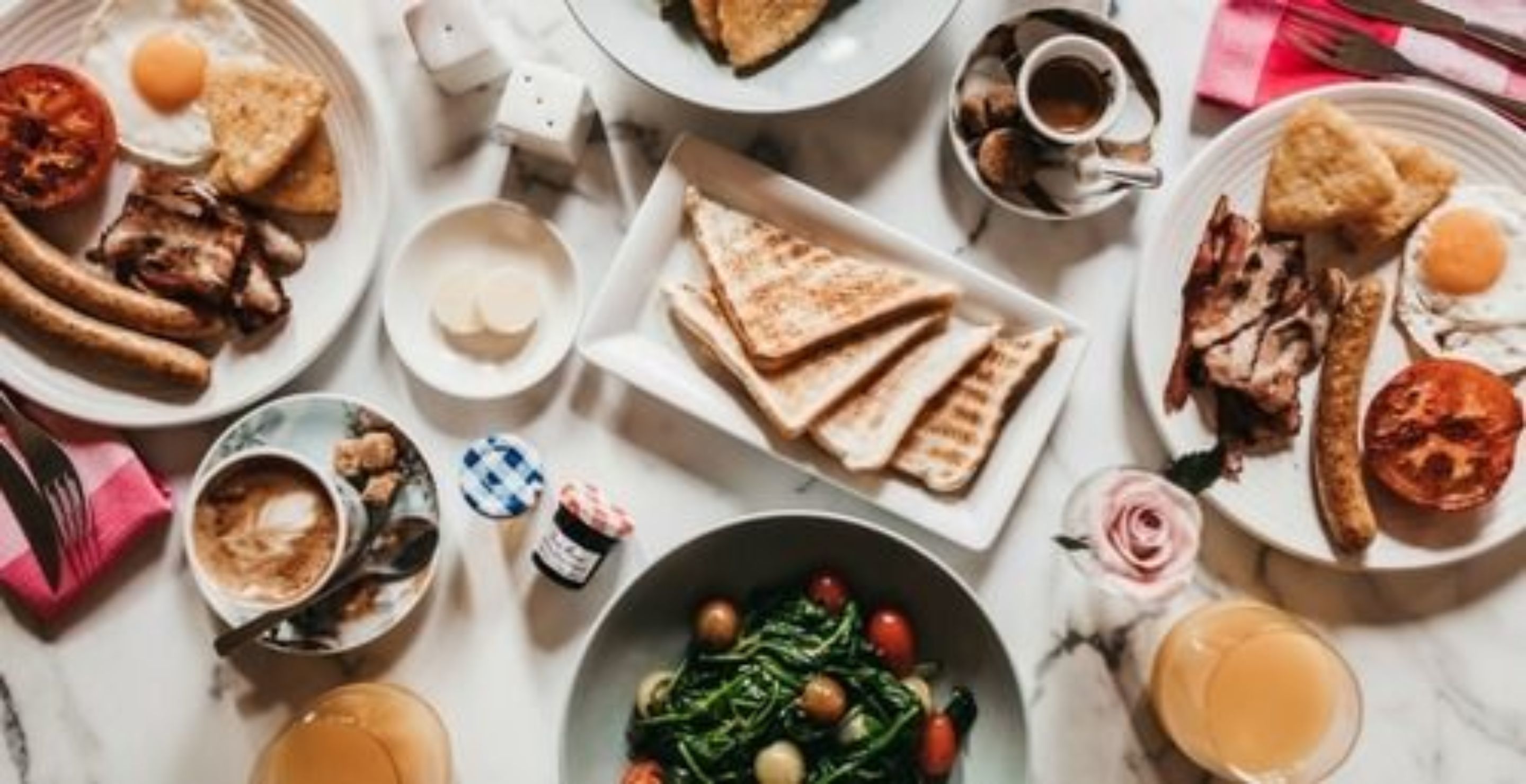 Un desayuno abundante con diversos platos, como huevos, tostadas, salchichas y un tazón de verduras.