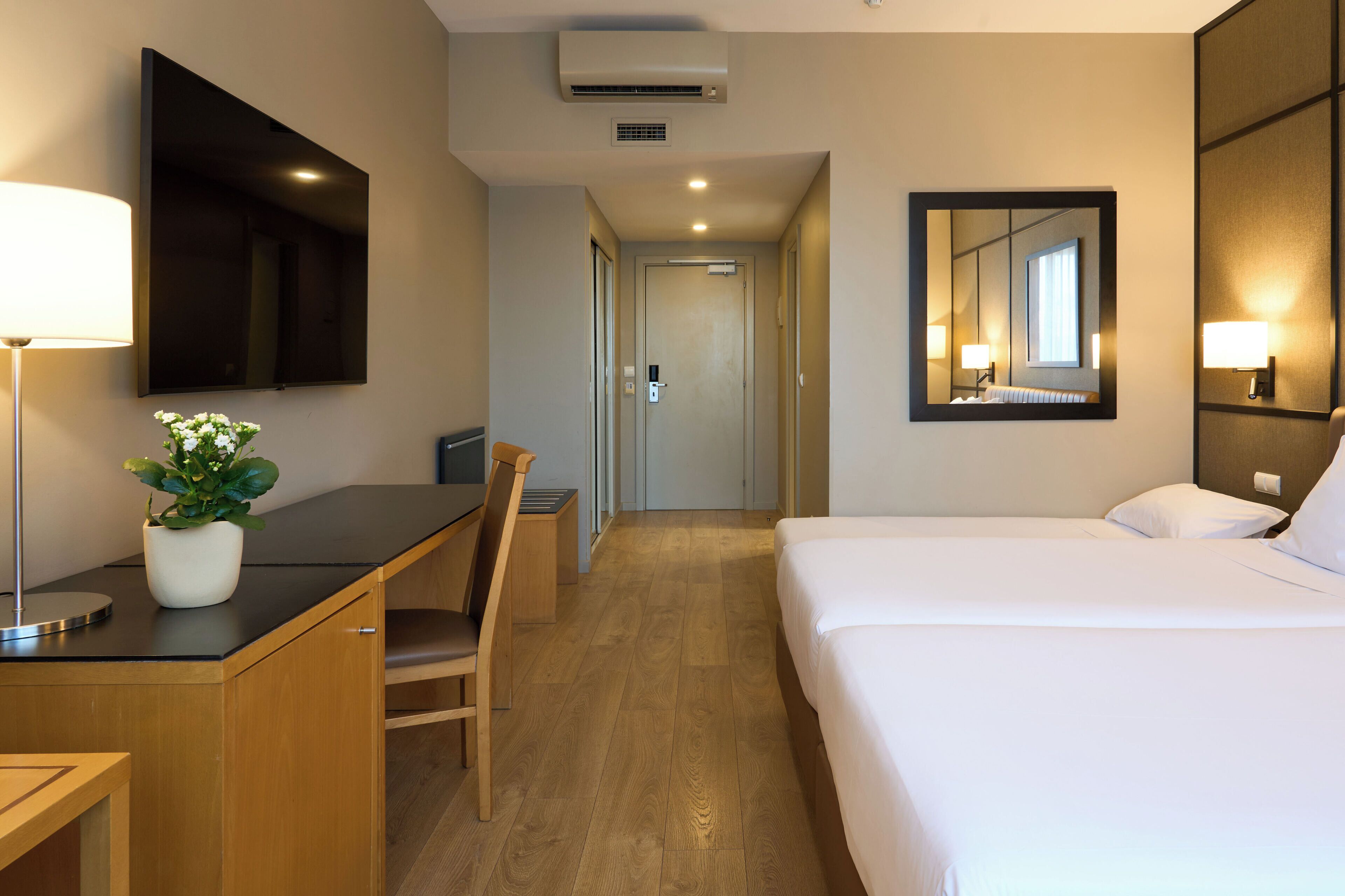 Een hotelkamer met een bed, een bureau, een stoel, een aan de muur bevestigde televisie en een spiegel.