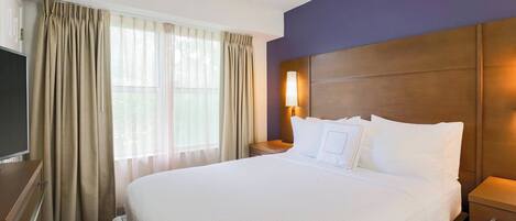 Una habitación de hotel con una cama grande, un televisor, una mesita de noche y una ventana con cortinas.