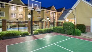 An outdoor basketball court with a net, surrounded by a fence and street lamps, adjacent to a building with a pool. - Residence Inn by Marriott Monroe (Monroe)
