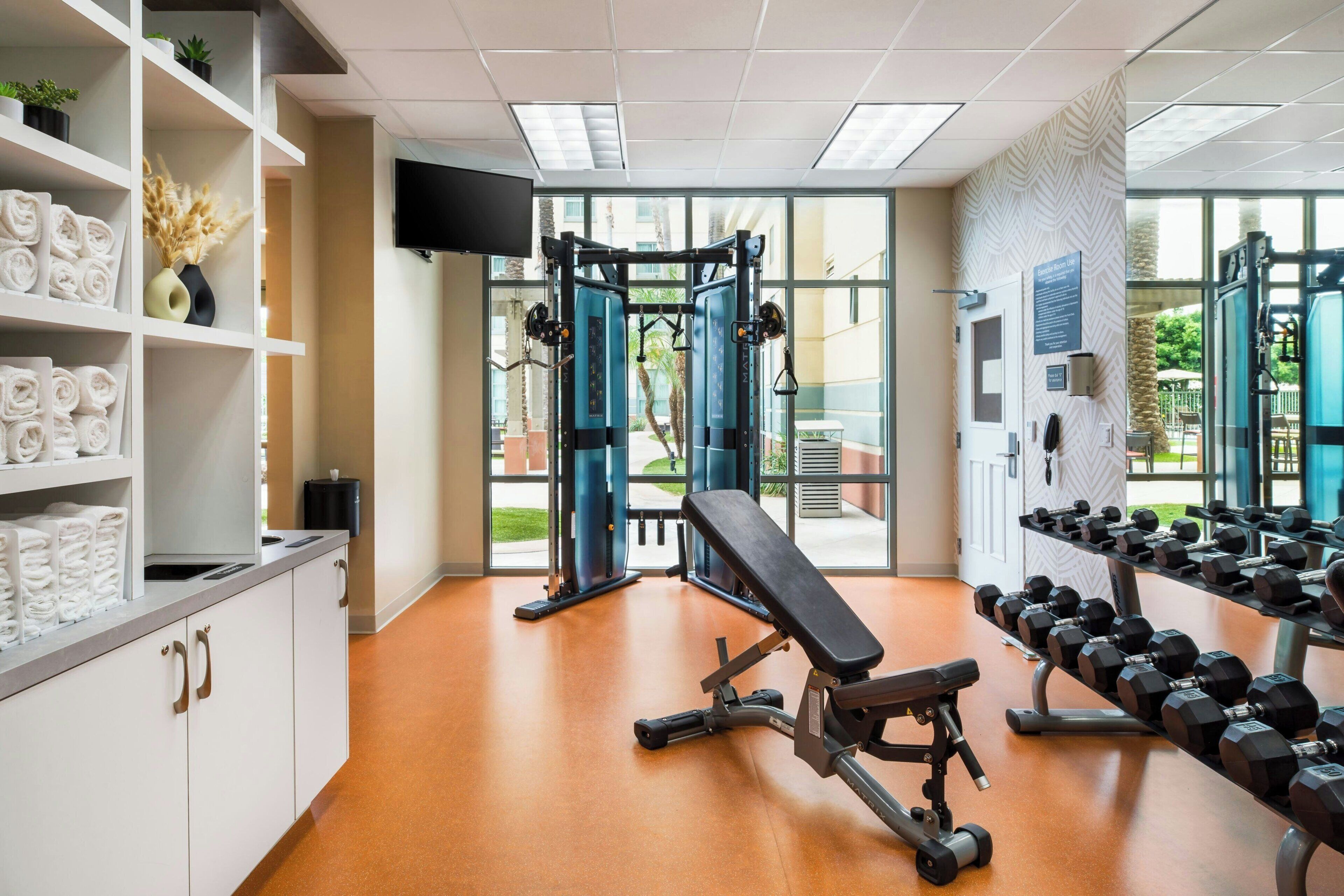 A gym with exercise equipment, a bench, and a wall-mounted TV.