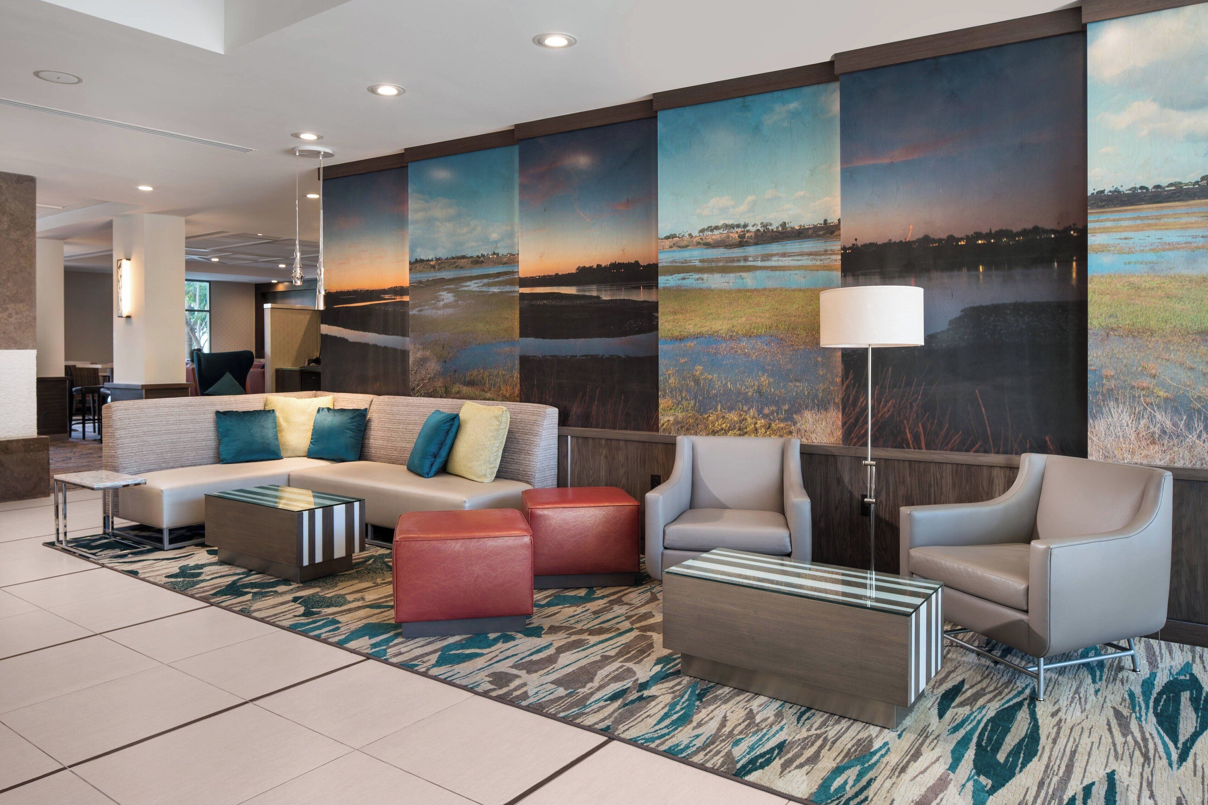 A modern lobby with a sofa, armchairs, a coffee table, and a large painting of a landscape.