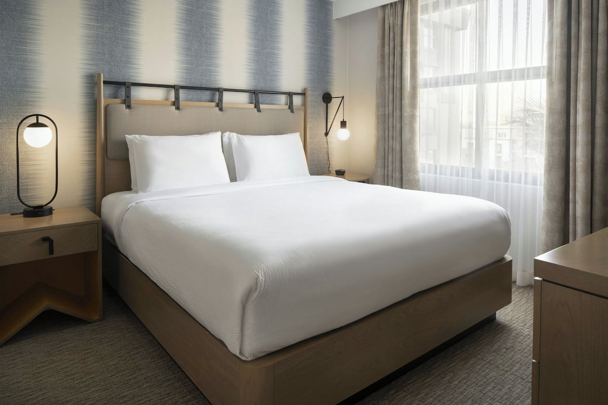A neatly made bed with a wooden headboard, two bedside tables with lamps, and a large window with curtains.