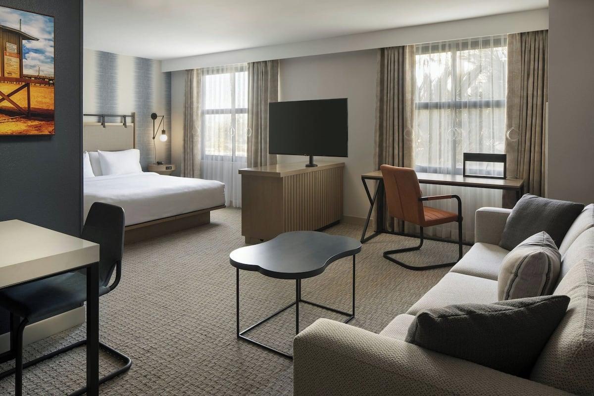 A hotel room with a bed, a desk, a TV, a sofa, and a chair.