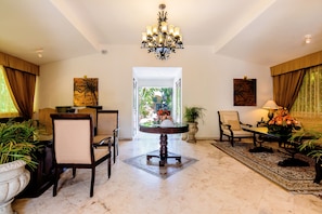A spacious living room with a round coffee table, several chairs, a chandelier, and a view of the outdoors.