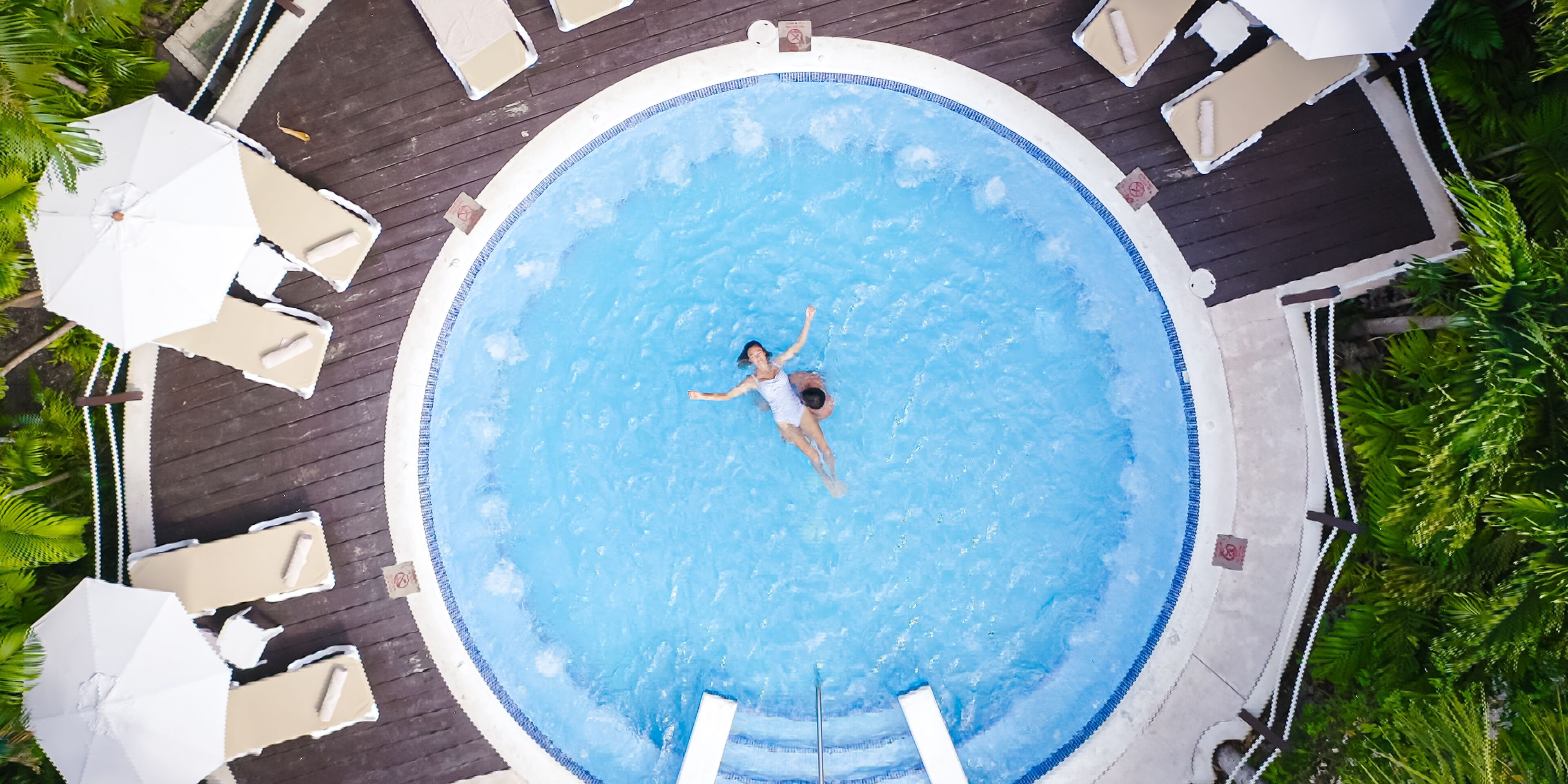 Una piscina rodona amb una persona nedant, envoltada de gandules i ombrelles.