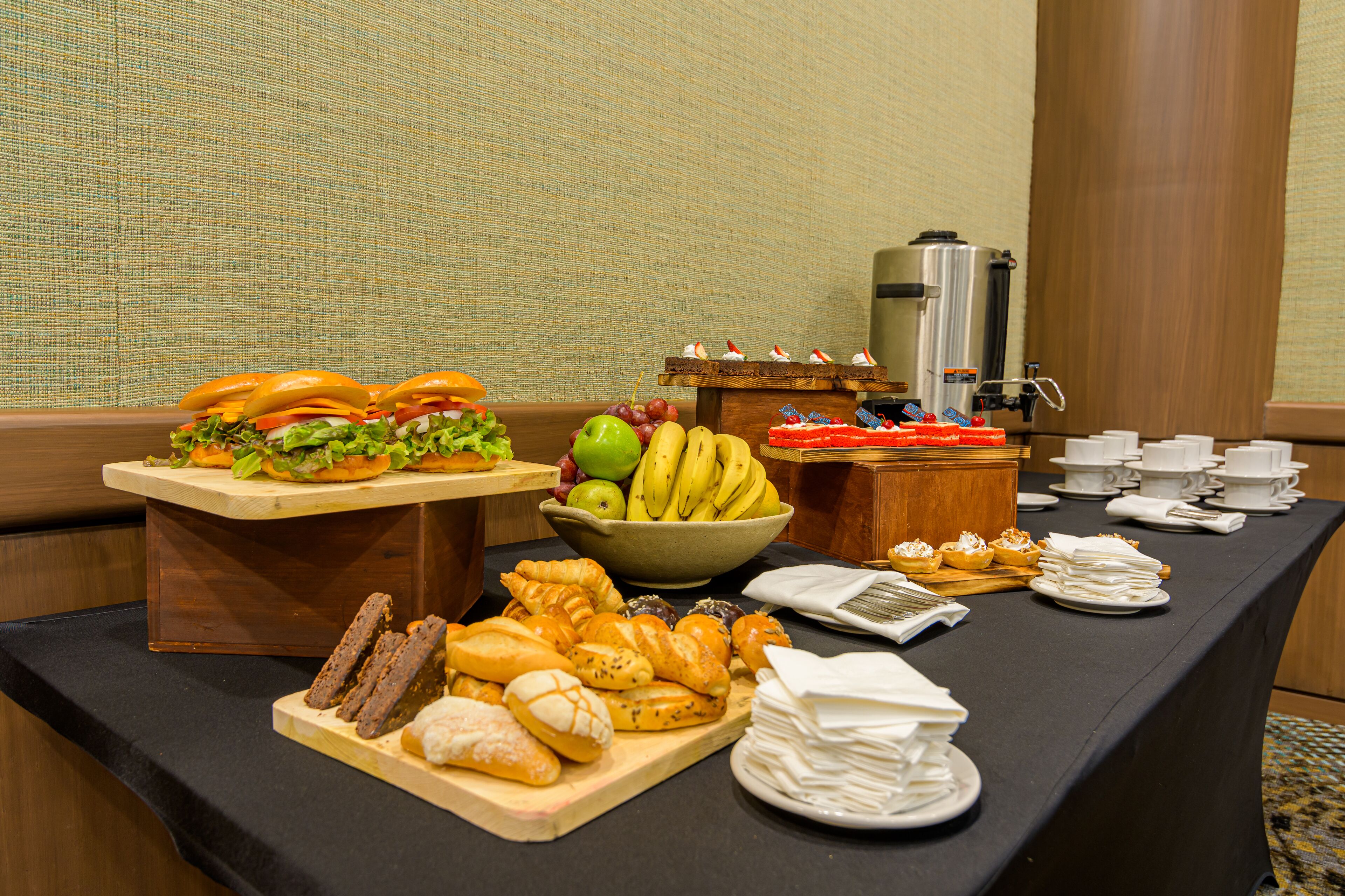 Una mesa de buffet con diferentes opciones de comida, como sándwiches, frutas, pasteles y una estación de café.