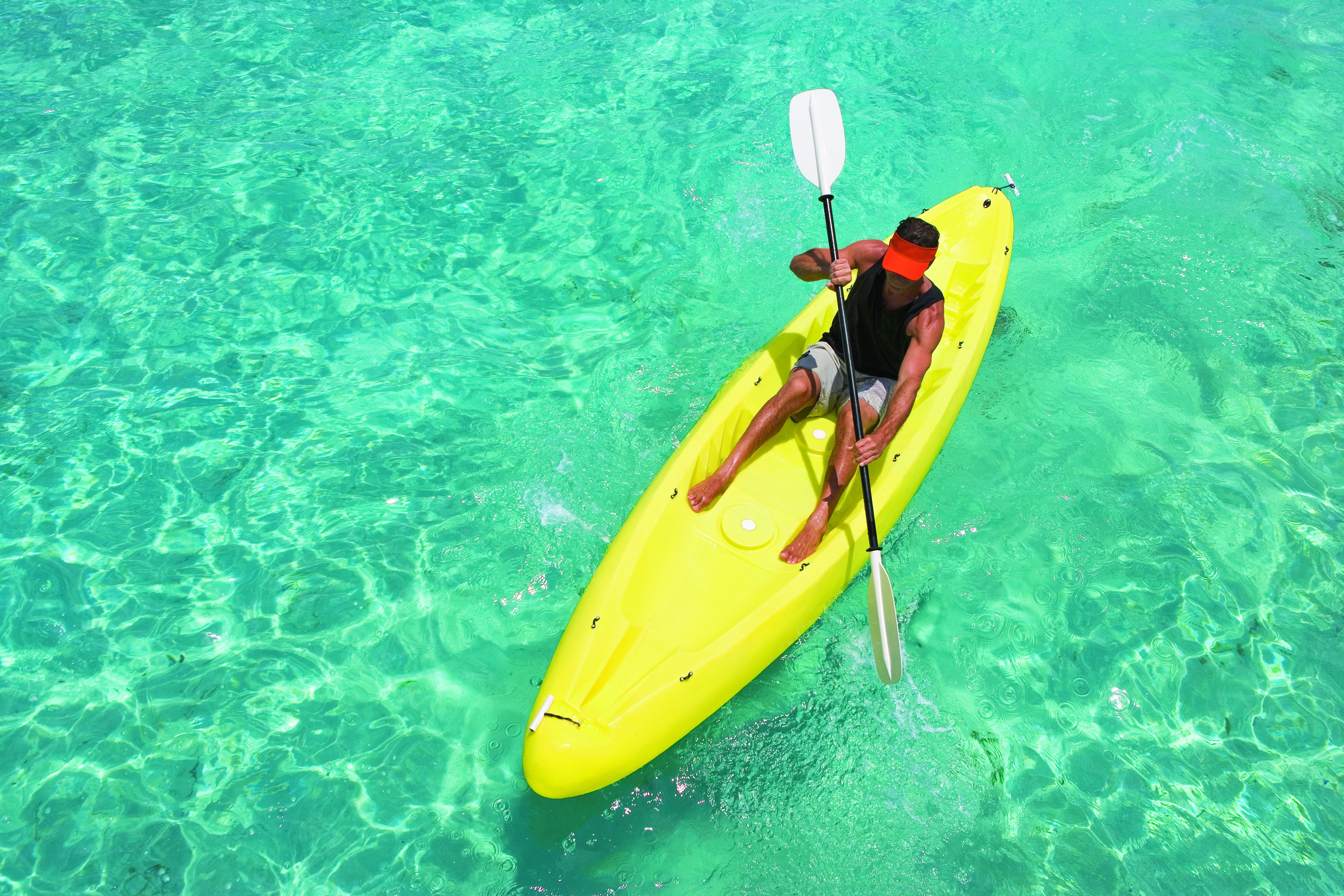 Una persona remar en kayak, un kayak amarillo brillante, en aguas claras y poco profundas.
