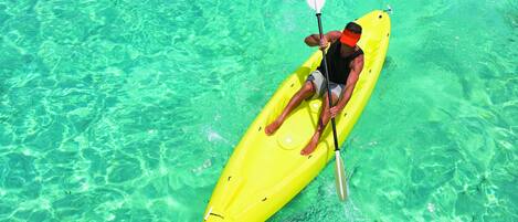 A person kayaking on a bright yellow kayak in clear, shallow water.