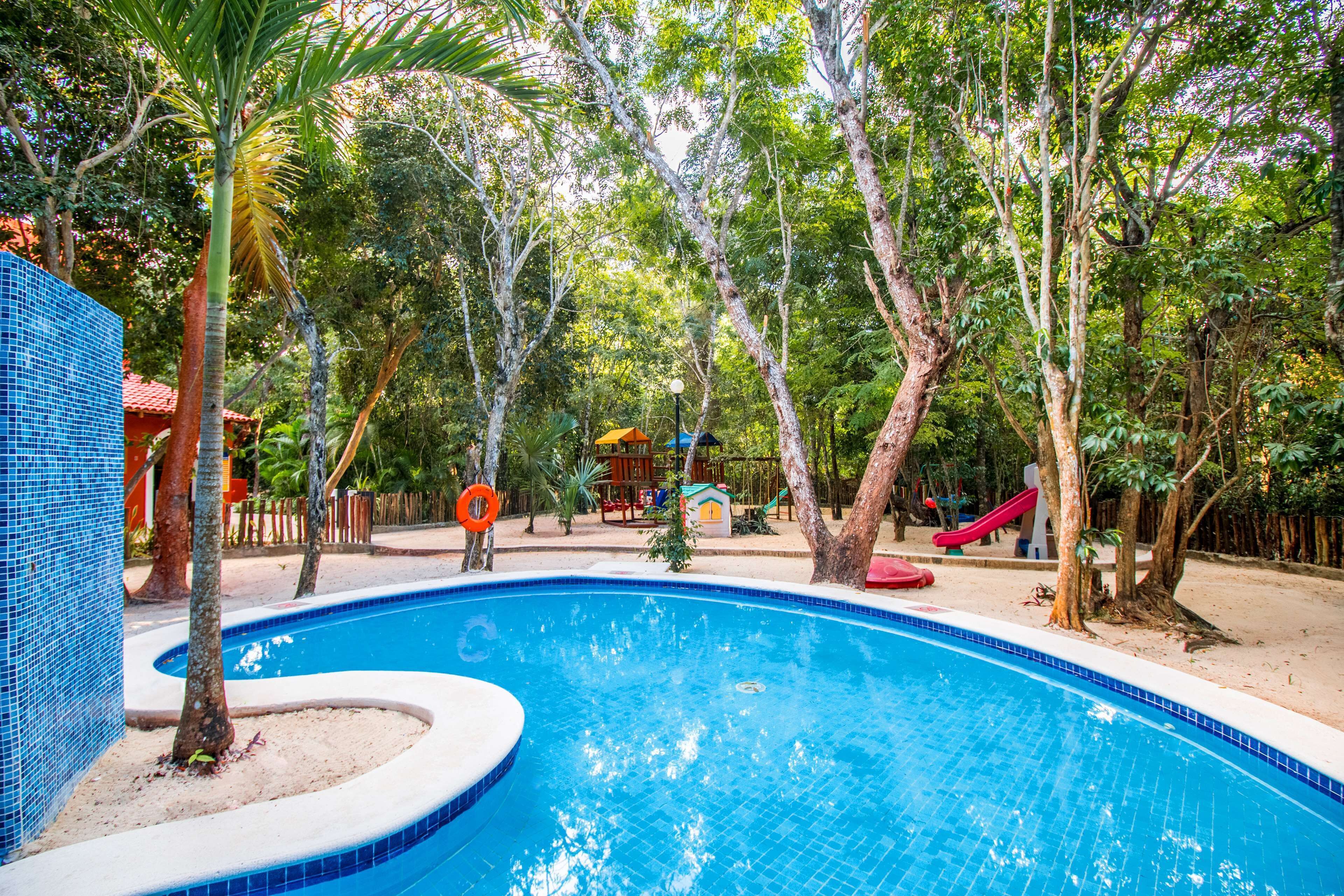 Piscina rodeada por árvores e um parquinho com escorregadores.