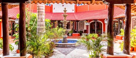 A courtyard with a fountain, potted plants, and a tiled floor.