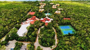 An aerial view of a resort with multiple buildings, a swimming pool, and a tennis court surrounded by dense greenery. - Occidental Cozumel - All Inclusive (Cozumel)