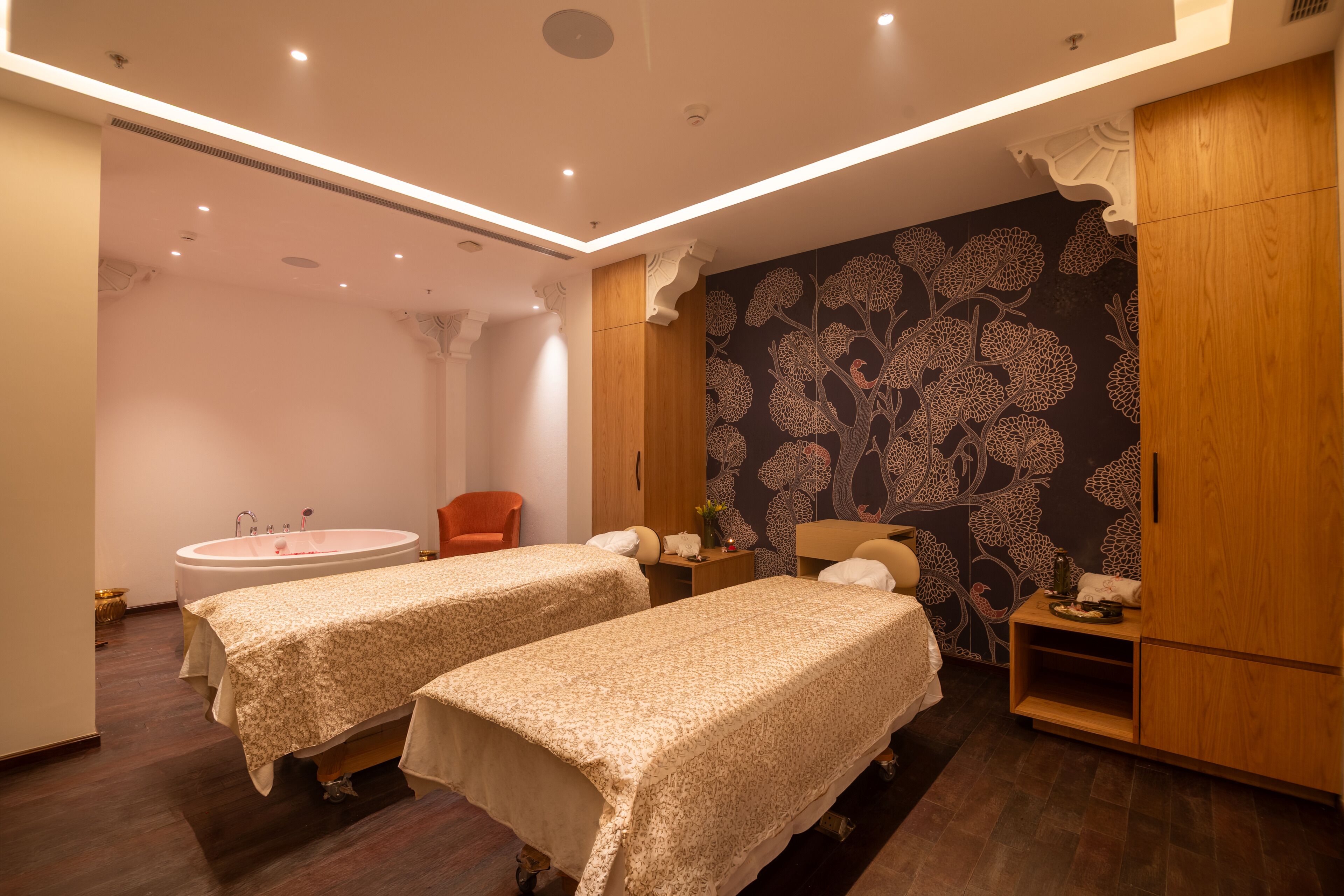 A room with two beds, a bathtub, a chair, and a wall with a floral pattern.