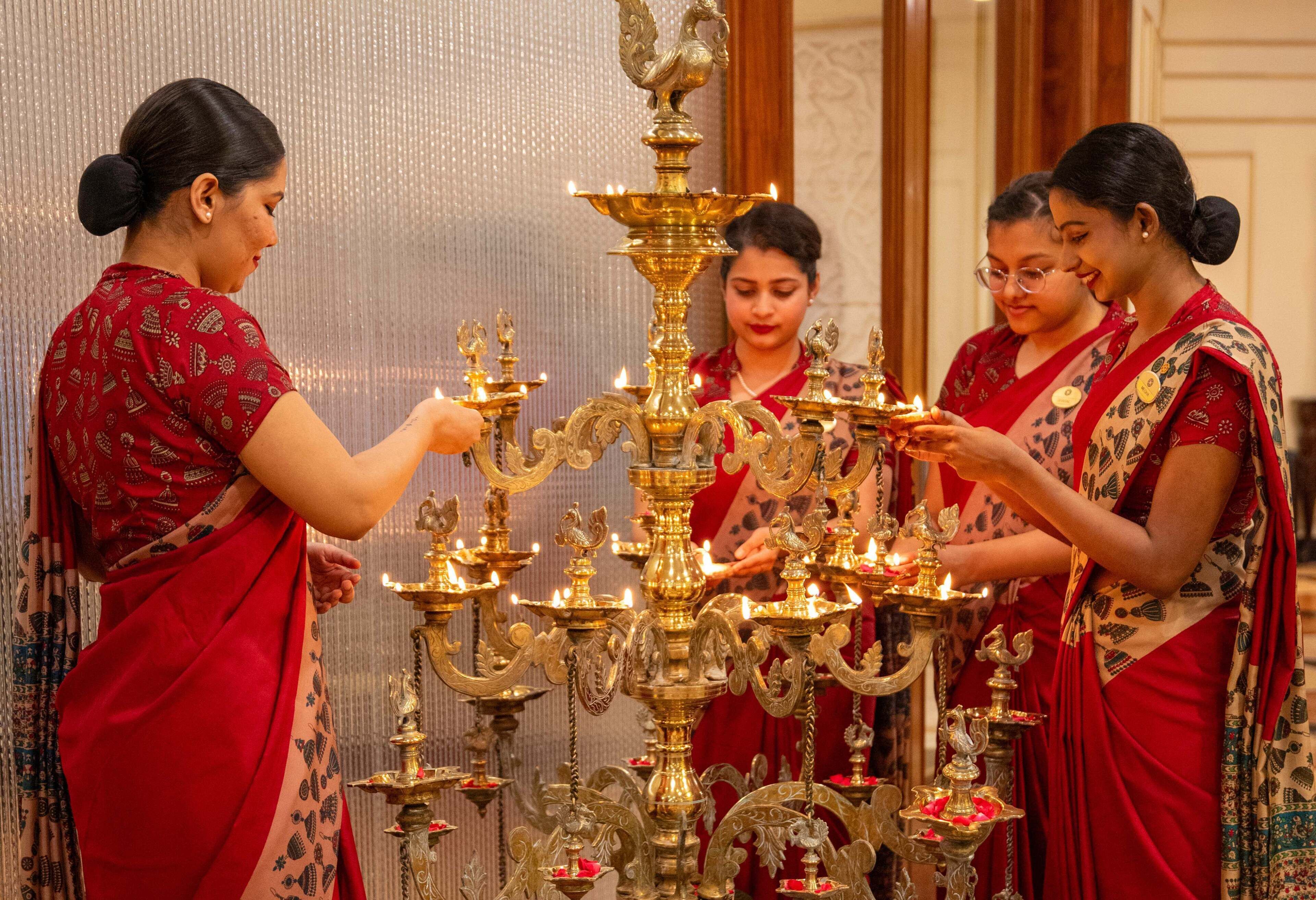 Un grupo de mujeres con vestimenta tradicional realizan un ritual con lámparas de aceite encendidas.