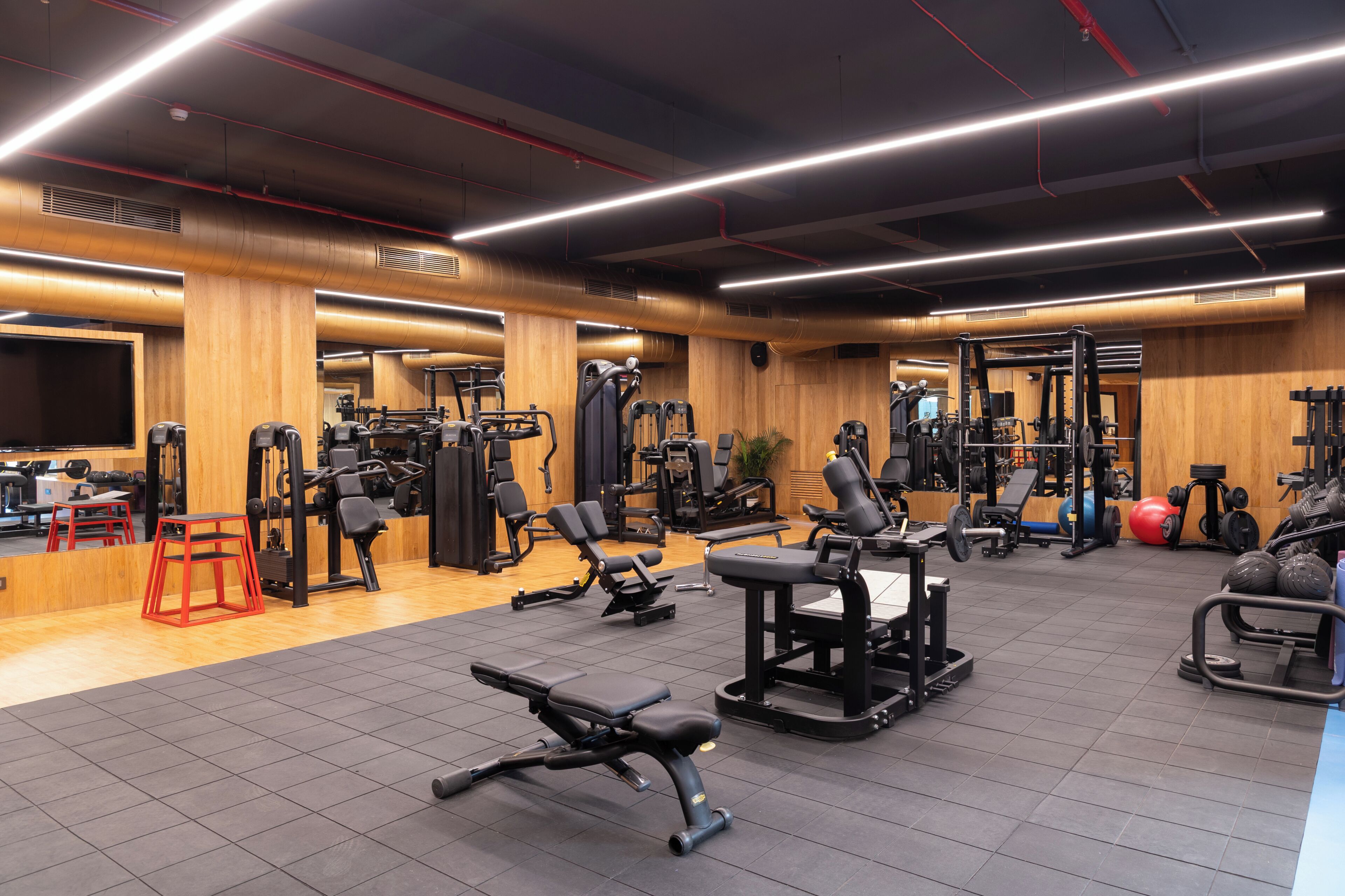 Ein Fitnessstudio mit unterschiedlicher Trainingsausstattung, Holzwänden und einem gefliesten Boden.