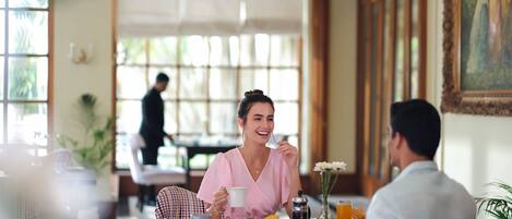 Comedor con una mesa para dos personas, alguien sosteniendo una taza y otra persona sentada al otro lado.