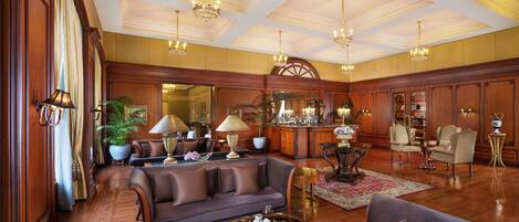A spacious living room with a large sofa, armchairs, a coffee table, and a bar area with a large mirror and decorative items.