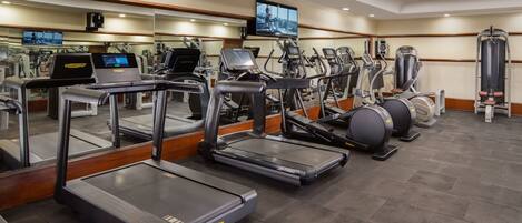 A gym with treadmills, elliptical machines, and a mirrored wall with a TV.
