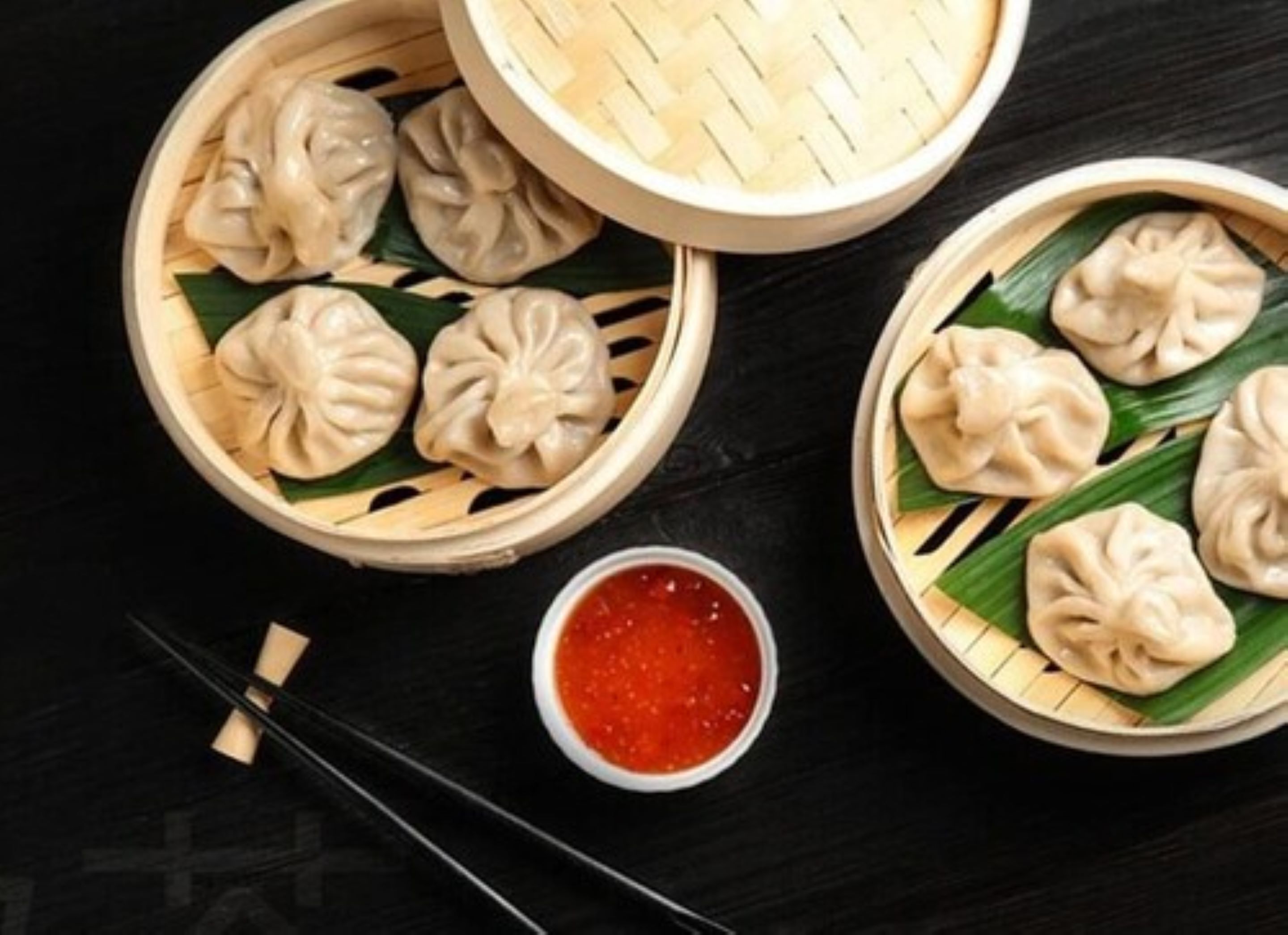 Two bamboo steamer baskets with dumplings on a dark surface.
