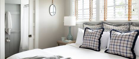 A neatly arranged bedroom with a bed, pillows, a nightstand, a lamp, and a window with blinds.