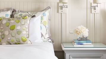 A neatly made bed with patterned pillows, a bedside table with a vase of flowers, and a stack of books.