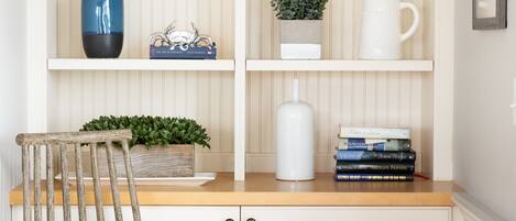A wooden chair with a cushion, a bookshelf with books and decorative items, and a white cabinet.