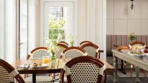 A dining area with a table set for breakfast, wicker chairs, and a view through a window. - Vineyard Square Hotel & Suites (Edgartown)