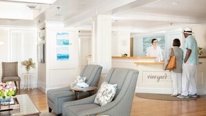 A reception area with a checkered sofa, a wicker chair, and a reception desk. - Vineyard Square Hotel & Suites (Edgartown)