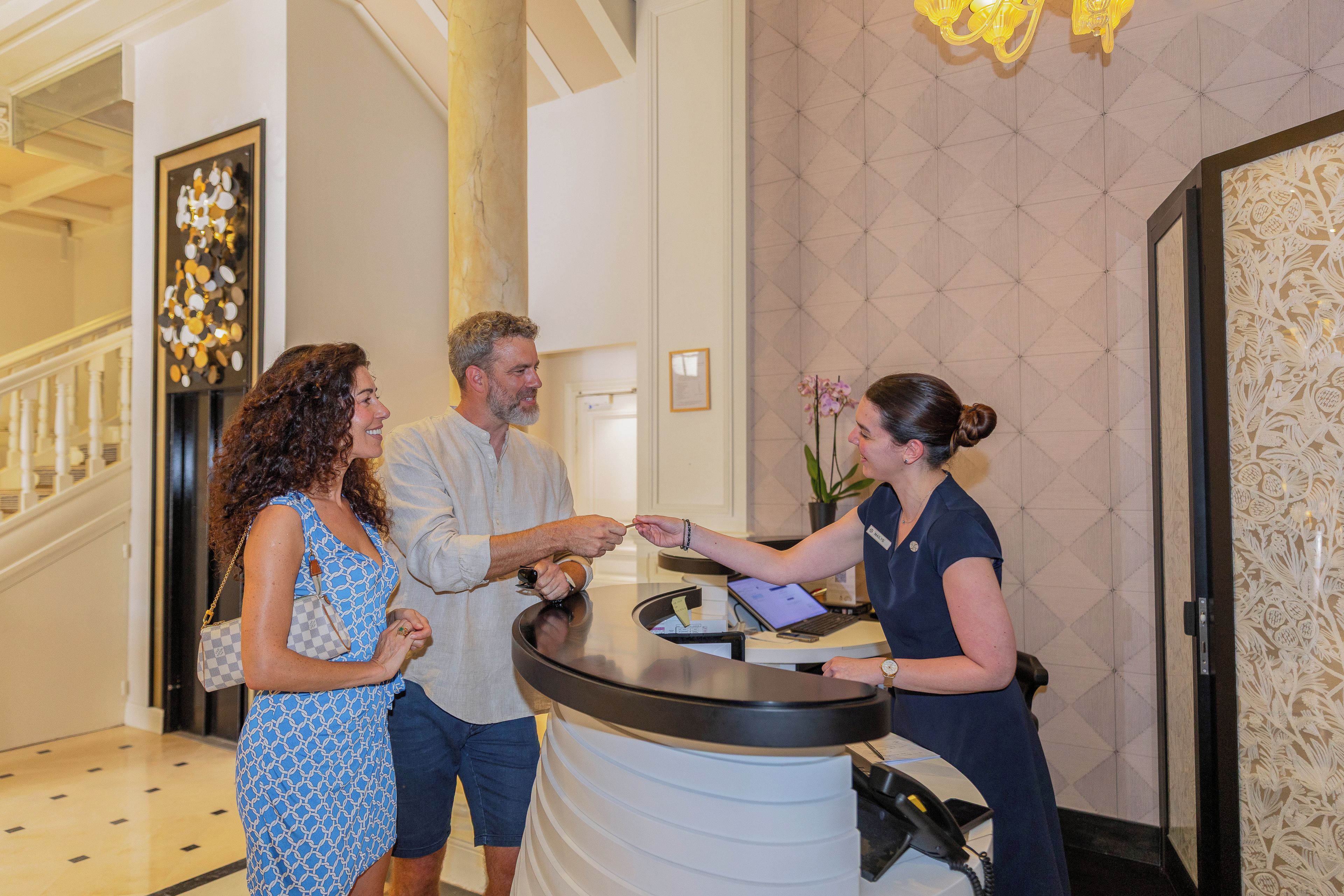Un mostrador de recepción en el vestíbulo de un hotel, con una columna de mármol, una escalera y una pared con diseño.