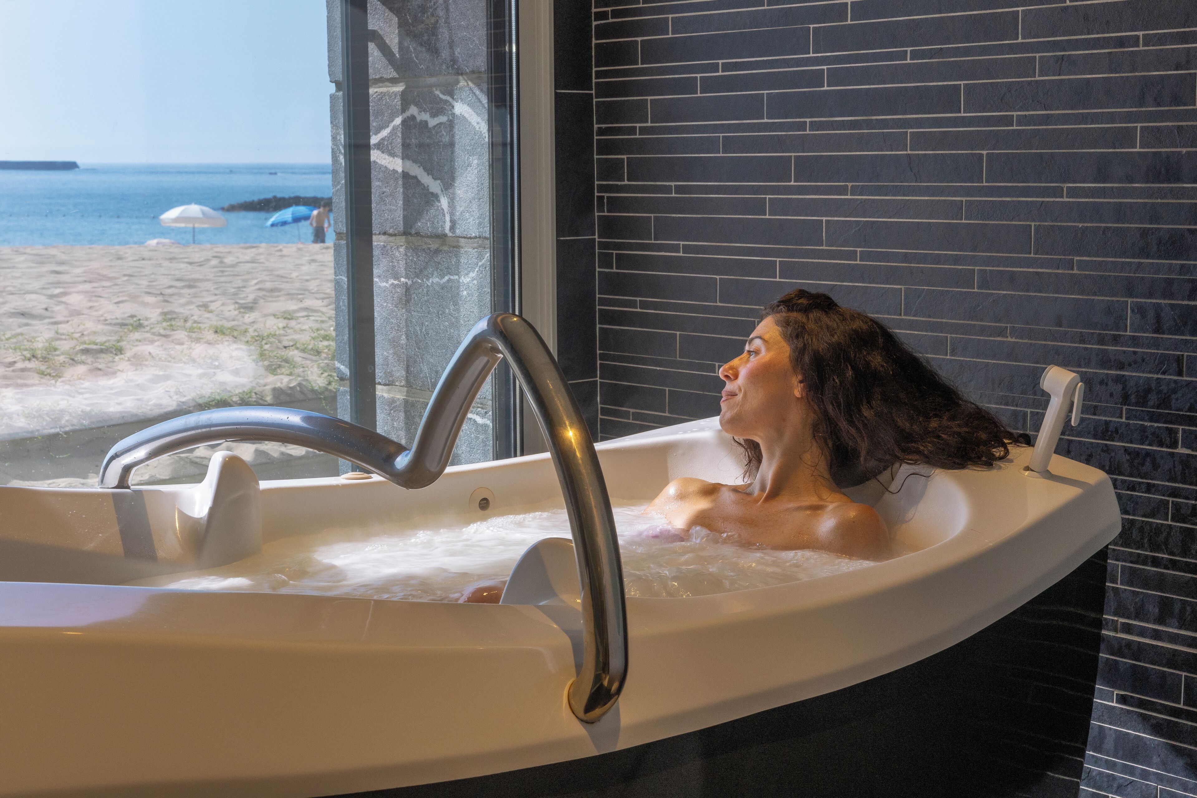 A bathtub with a view of the beach and ocean through a large window.