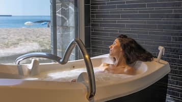 A bathtub with a view of the beach and ocean through a large window.