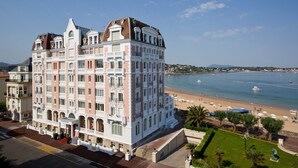 A large, multi-story hotel with a prominent balcony on the second floor, situated near a beach with a clear view of the sea. - Grand Hôtel Spa & Thalasso à Saint-Jean-de-Luz (Saint-Jean-de-Luz)
