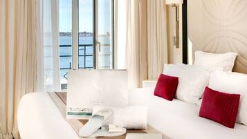 A hotel room with a bed, a window with a view of the sea, a towel, slippers, and a brochure.