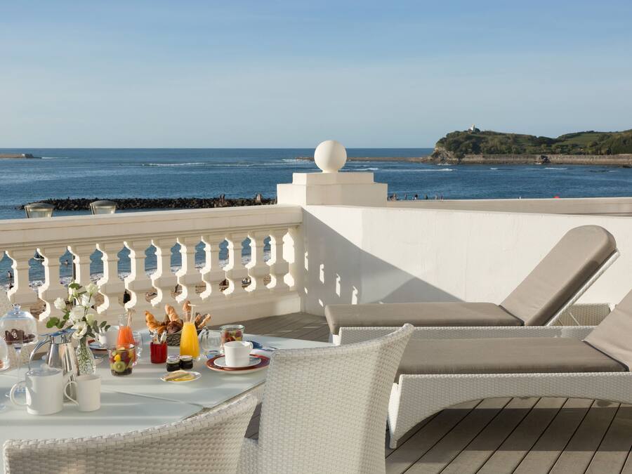 Une terrasse meublée de mobilier en osier, une table dressée pour le petit-déjeuner et une vue sur la mer.