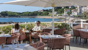 An outdoor dining area with tables and chairs, overlooking a beach and ocean. - Grand Hôtel Spa & Thalasso à Saint-Jean-de-Luz (Saint-Jean-de-Luz)