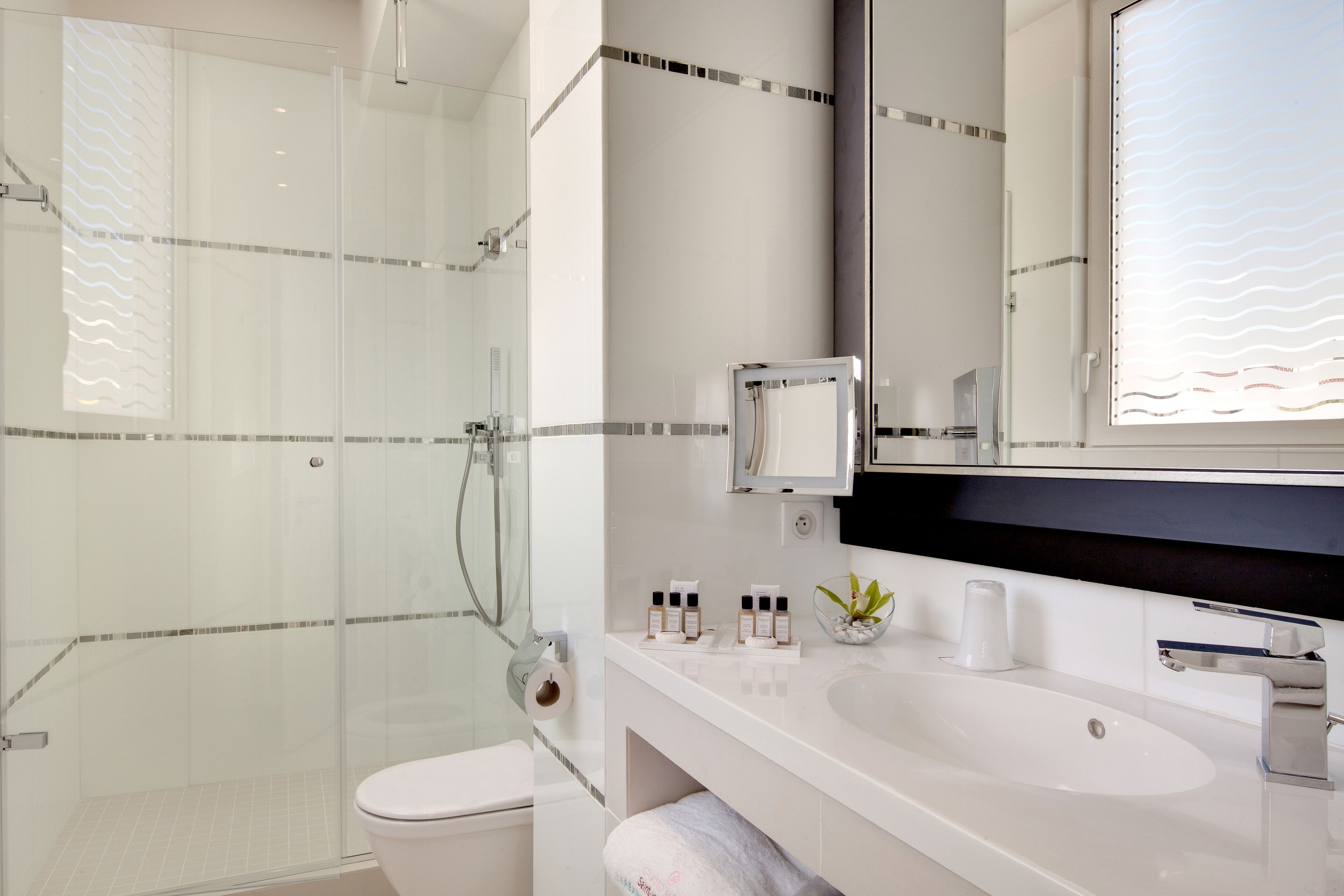 A modern bathroom with a glass shower enclosure, a white sink, and a large mirror.