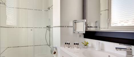 Une salle de bain moderne avec une douche à parois de verre, un lavabo blanc et un grand miroir.