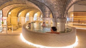 An indoor swimming pool with stone arches, a seating area, and a modern interior. - Grand Hôtel Spa & Thalasso à Saint-Jean-de-Luz (Saint-Jean-de-Luz)