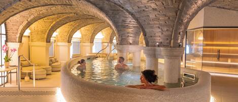 Una piscina interior con arcos de piedra, zona de estar y diseño moderno.