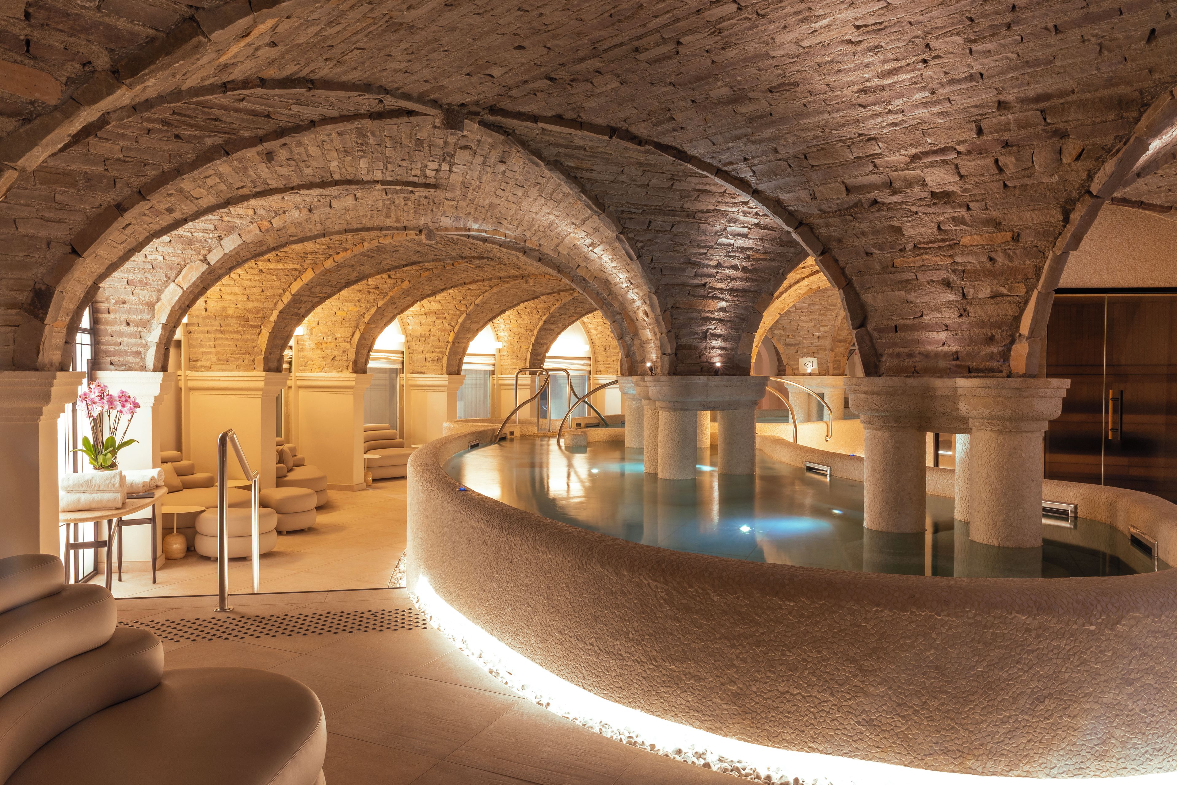 Ein Wellnessbereich mit einem Steinbecken, Gewölbedecken und Sitzgelegenheiten.